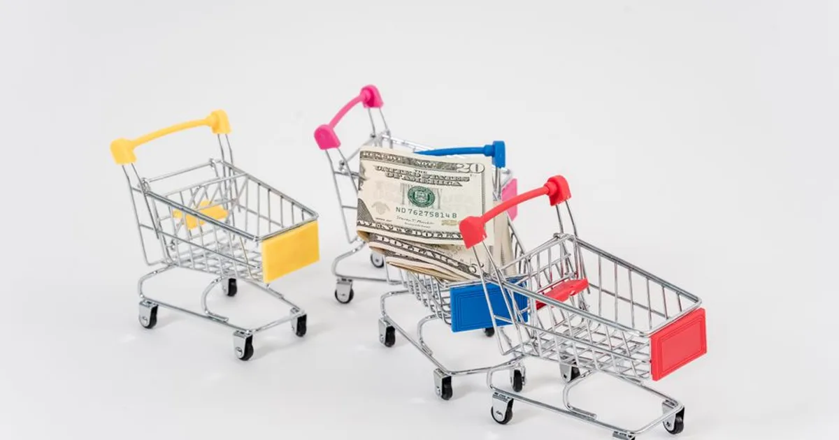 Colorful miniature shopping carts with dollar bills, symbolizing consumerism and finance.