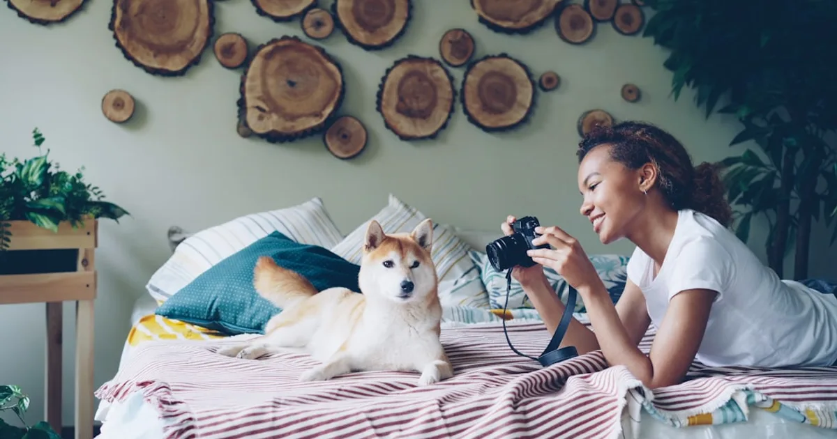 Woman takes a photo of a dog on a bed.