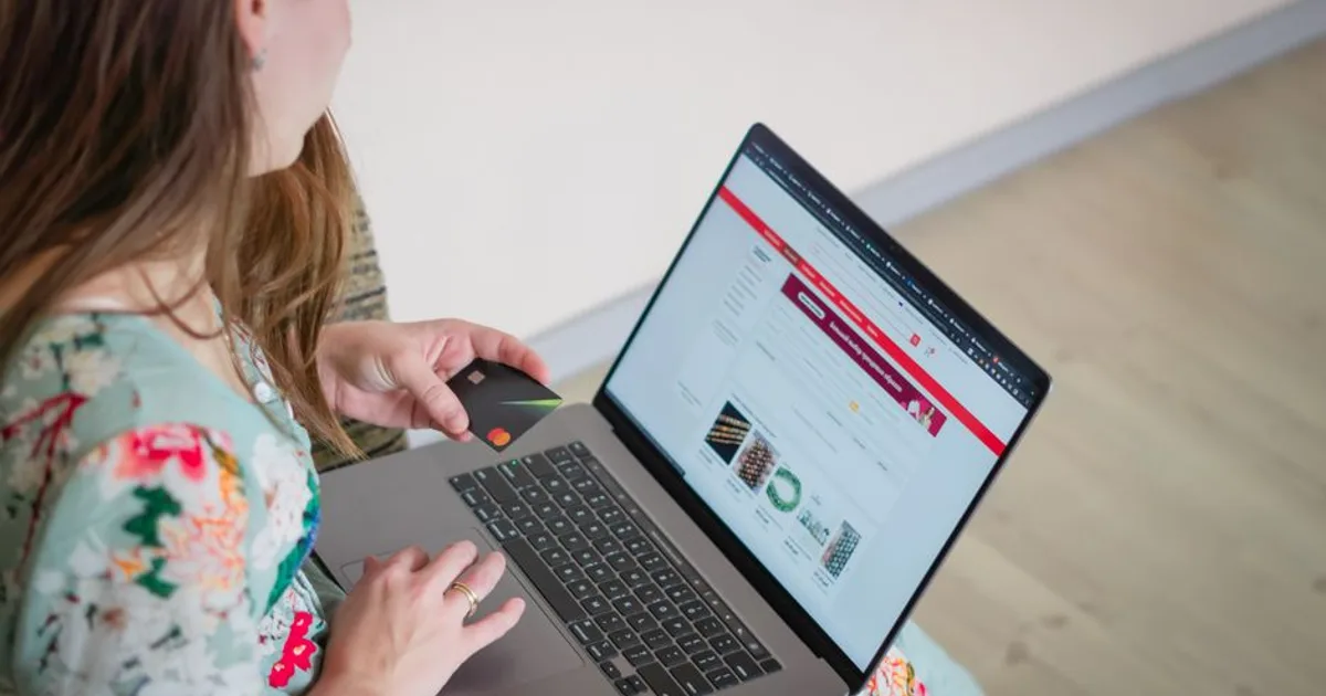 Woman in floral dress shopping online with a laptop and credit card indoors.