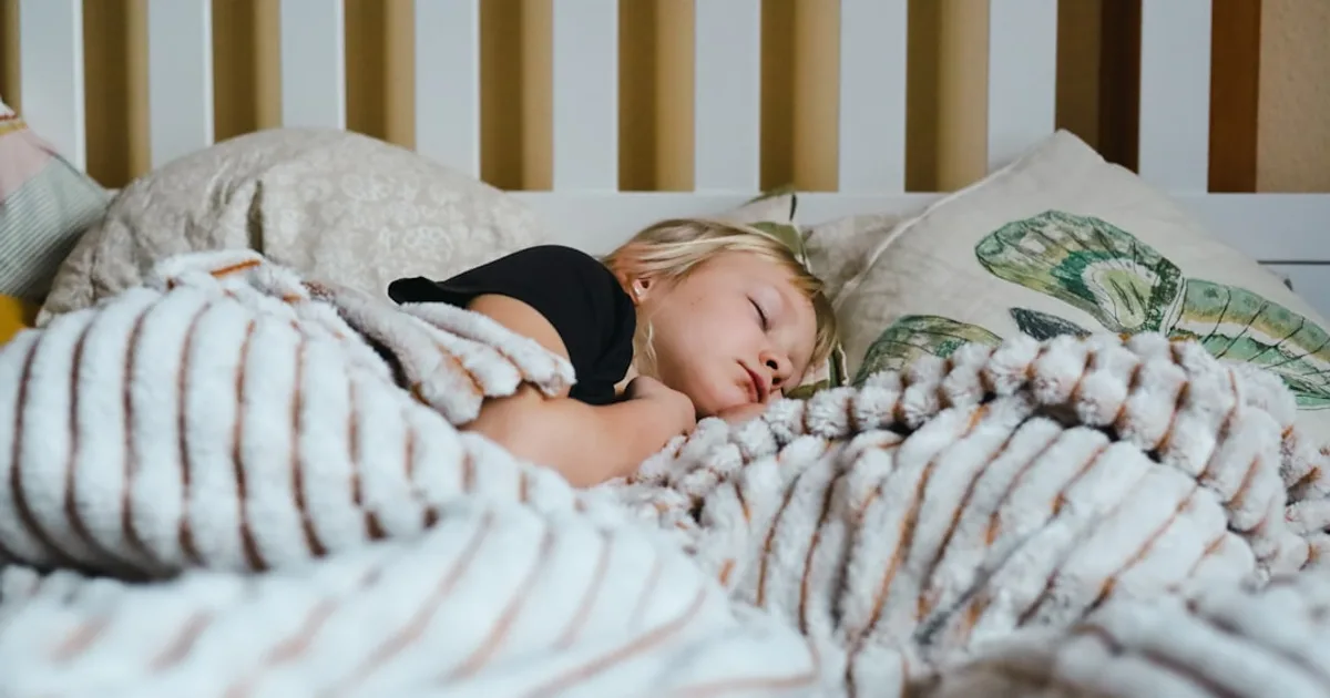 a little girl sleeping in a bed with a blanket