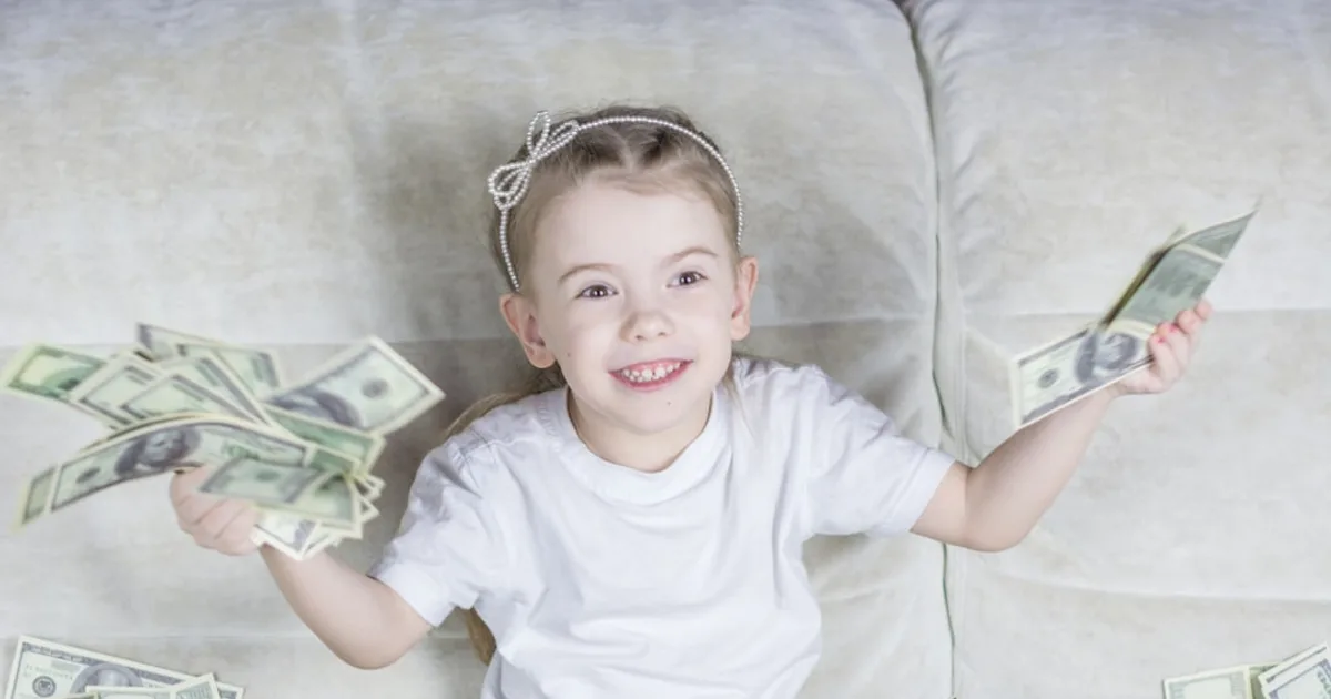a little girl sitting on a couch holding money