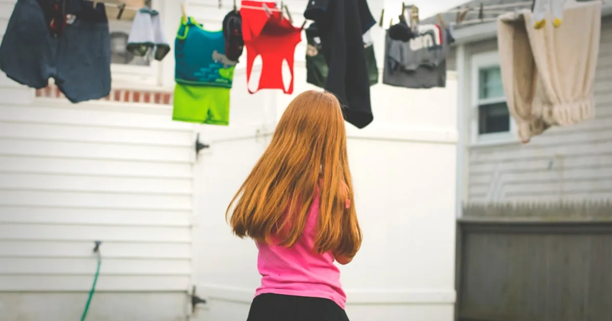 girl standing under clothes on airer at daytime