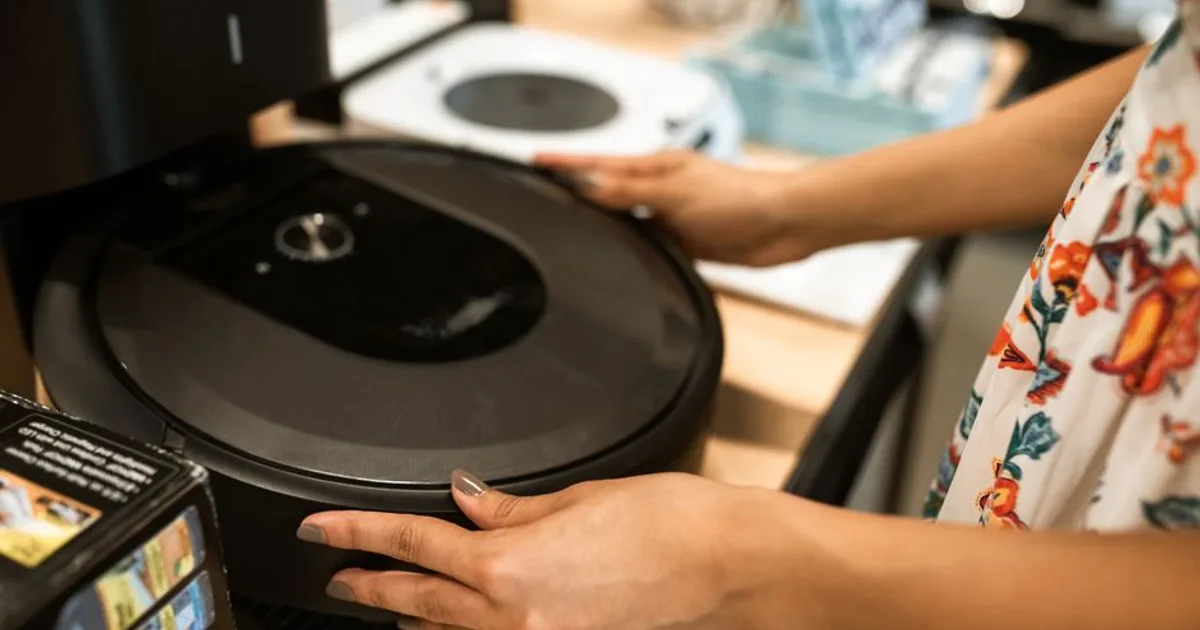 A customer examines a sleek robotic vacuum cleaner in a modern store.