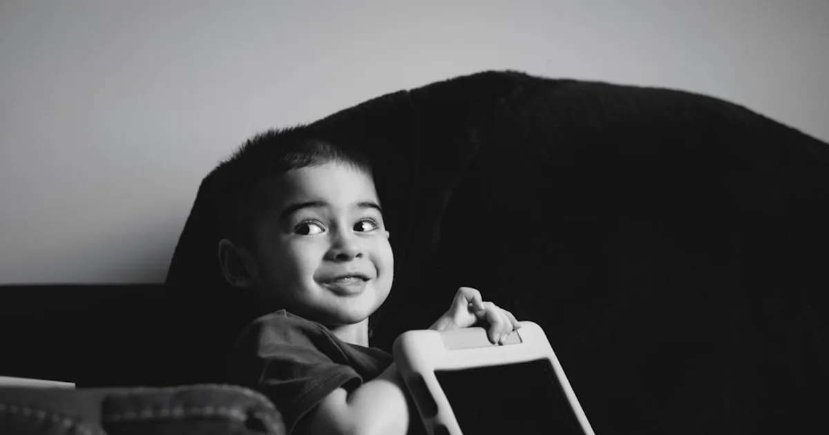 A young boy smiles while holding a tablet.